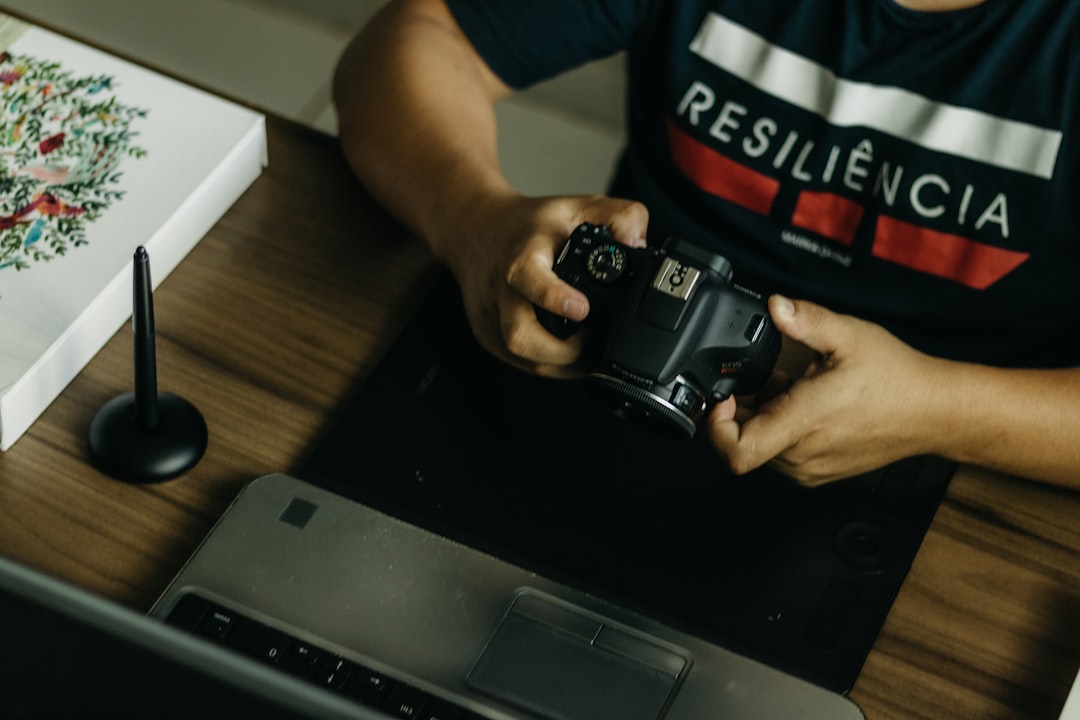 a man sitting at a desk holding a camera — Photo by Kawê Rodrigues on Unsplash