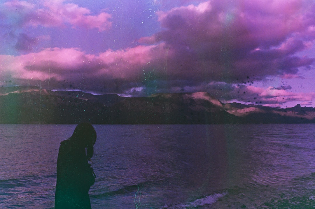 a person standing in front of a body of water with a mountain in the background — Photo by melanie nobaru on Unsplash