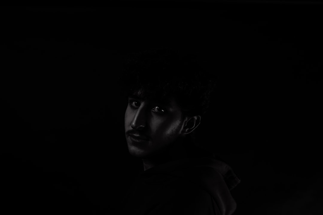 A man standing in the dark with his head turned to the side — Photo by Erfan Khoshbin on Unsplash